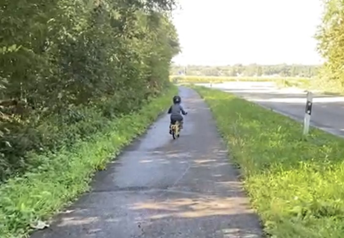 Ein Kind fährt von hinten gesehen auf einem Fahrrad über einen gepflasterten Radweg in Deutschland.